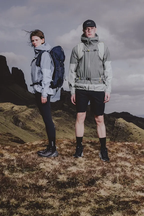 Zwei Wandernde in Outdoorjacken und Wanderschuhen stehen in einer felsigen Berglandschaft unter Wolkenhimmel